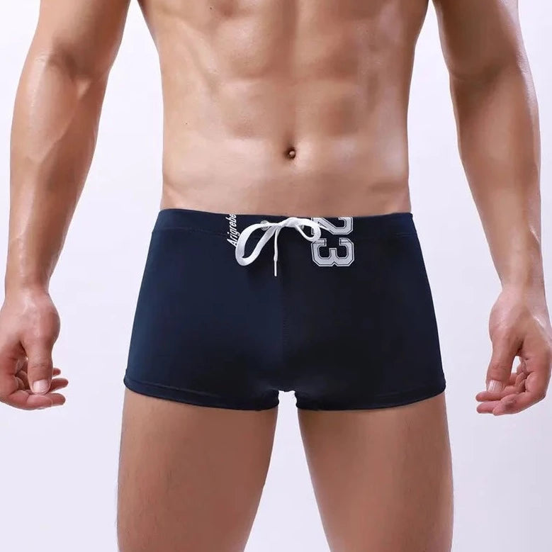 a hot gay man in dark blue Men's 23 Bowtie Swim Trunks - pridevoyageshop.com - gay men’s underwear and swimwear