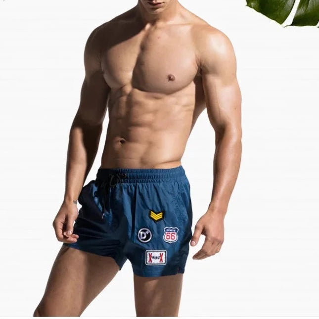 a hot gay man in blue Desmiit Travelers Board Shorts - pridevoyageshop.com - gay men’s underwear and swimwear