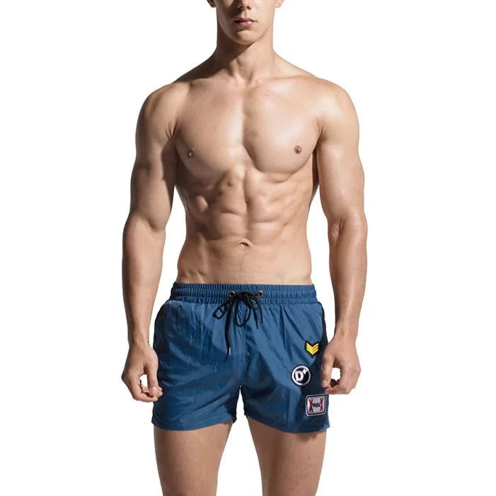a hot gay man in blue Desmiit Travelers Board Shorts - pridevoyageshop.com - gay men’s underwear and swimwear