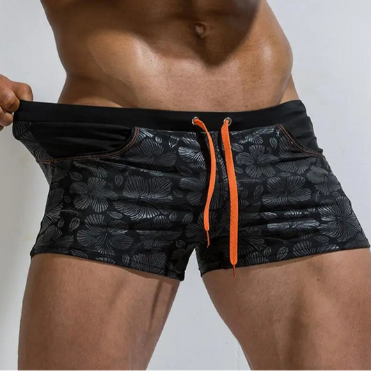 a sexy man in black Men’s Shiny Blossom Swim Trunks- pridevoyageshop.com - gay men’s sexy swim briefs, trunks, board shorts, and bikinis