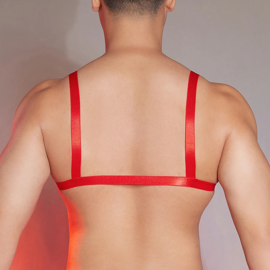 a sexy man in red faux-leather bralette with front clasp, shiny chest panel and sultry fetish energy, bold gay lingerie look – pridevoyageshop.com – gay men’s harness, lingerie and fetish wear