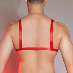 a sexy man in red faux-leather bralette with front clasp, shiny chest panel and sultry fetish energy, bold gay lingerie look – pridevoyageshop.com – gay men’s harness, lingerie and fetish wear
